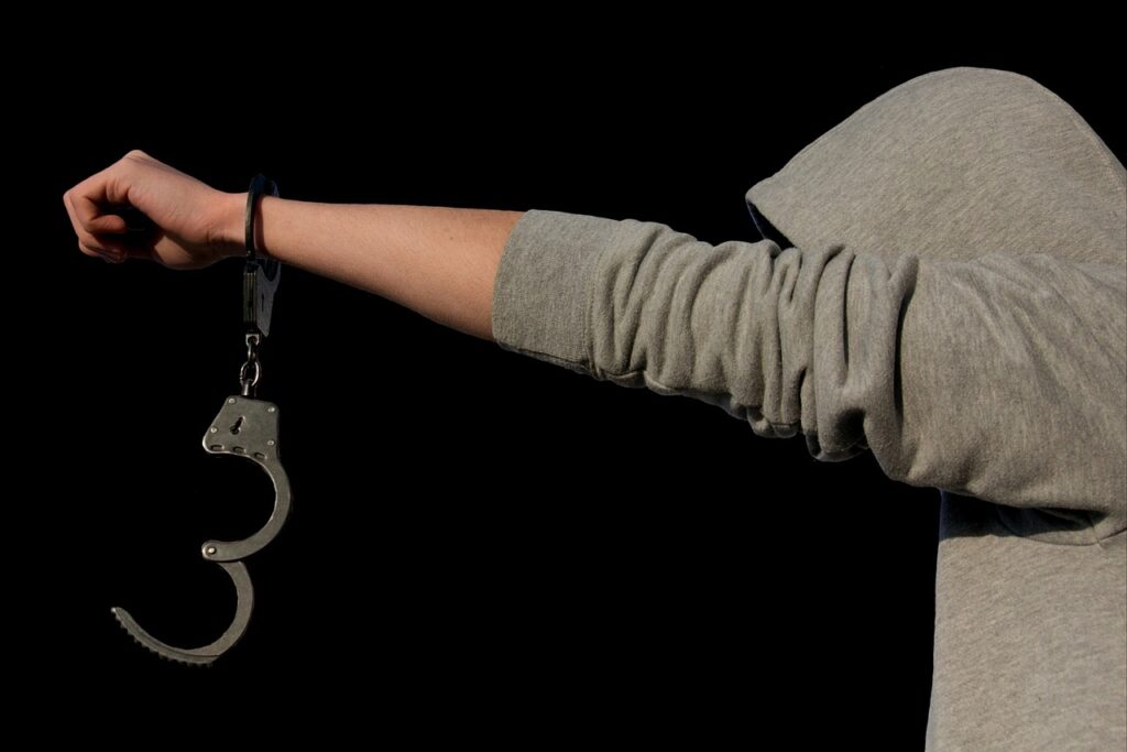 Persona con capucha extendiendo la mano, con unas esposas colgando